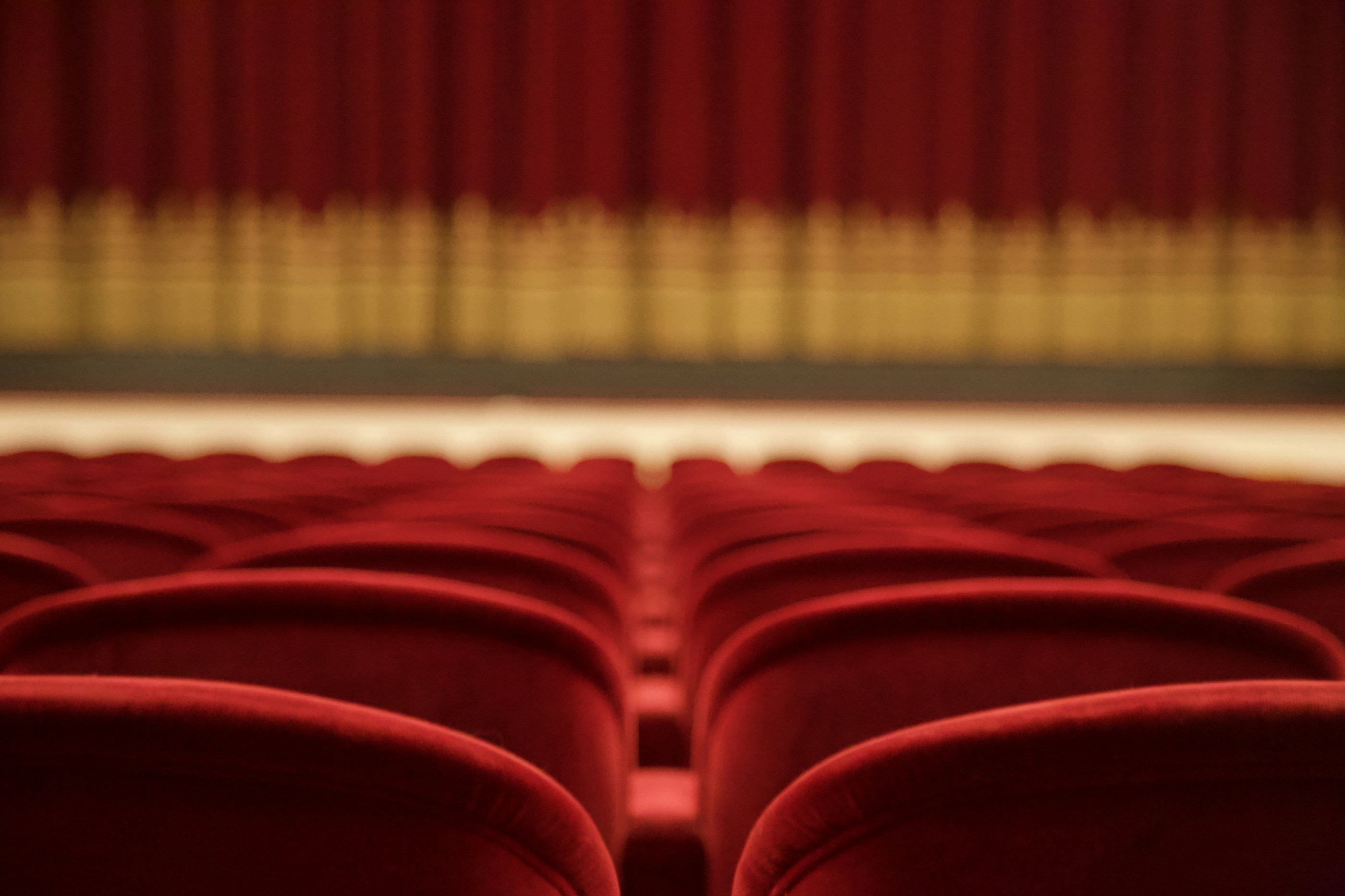 Rote Theatersessel mit Blick auf den geschlossenen Bühnenvorhang